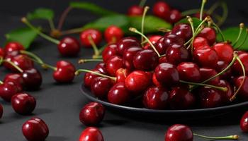 cerezas rojas maduras en un plato de cerámica sobre una mesa de madera negra foto