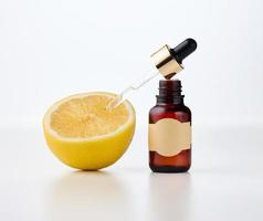 a brown glass bottle with an empty paper label and a pipette, next to it is half a lemon on a white front. Fruit acids in cosmetics photo