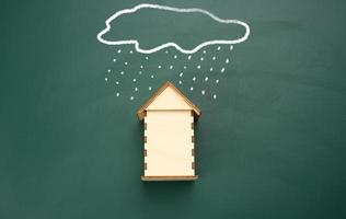 a wooden house and a drawn cloud with rain with white chalk on a green chalk board. photo