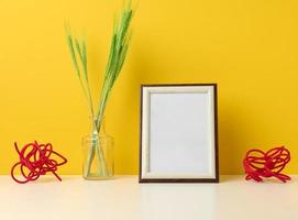 empty white wooden photo frame and green plants on white table, yellow background