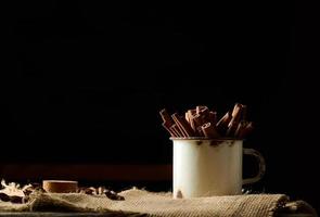 palitos de canela en una vieja taza de metal sobre una mesa negra. especia aromática foto