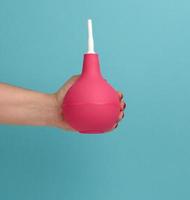 a hand in a blue medical glove holds a pink rubber enema on a blue background photo