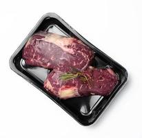 two raw beef steaks in a plastic container with spices and vacuumized on a white background, packaging for long-term storage
