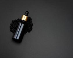 botella de vidrio con una pipeta yace sobre un montón de caviar negro, fondo negro. comedia natural. marca de producto foto