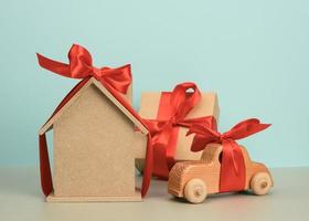 model of a wooden house tied with a red silk ribbon and a wooden car on a blue background, the concept of purchase photo