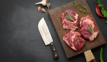 raw piece of beef ribeye with rosemary, thyme on a black table, top view photo