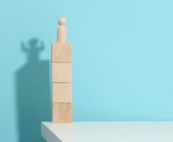 wooden figurine of a man stands high on the cubes, the shadow of a strong and victorious. Everyone is stronger than he thinks, a superhero. Blue background photo