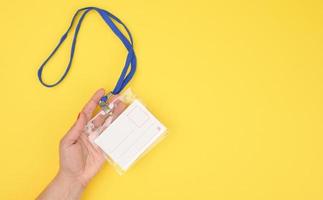 female hand holds transparent plastic badge on a blue lanyard on a yellow background photo