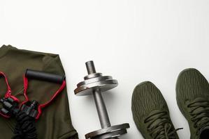 pair of green textile sneakers and a metal dumbbell on a white background, top view. Shoes for sports photo