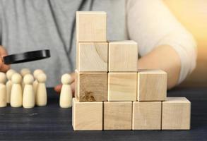 ladder of wooden cubes on a steel, behind a man under a magnifying glass examines wooden figures. Recruitment concept photo