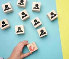 la mano femenina sostiene un cubo de madera con un imán y cubos de madera con hombres pequeños, reclutando para un equipo fuerte. vacantes abiertas en la empresa foto