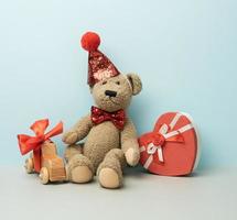 caja de regalo y oso de peluche marrón con una gorra roja sobre un fondo azul foto