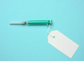 plastic syringe and attached white paper tag on blue background photo