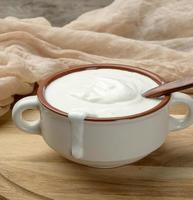 sour cream in a brown ceramic bowl with a wooden spoon on a wooden board photo