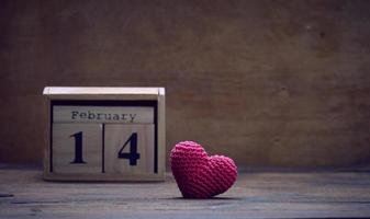 wooden calendar with date February 14 and red knitted heart, brown background photo