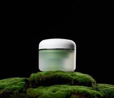 round green plastic jar with white lid for cosmetics stands on green moss, black background. Natural creams and masks. Product branding photo