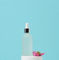 botella de vidrio blanco con soportes de pipeta sobre un fondo azul. marca de spa de cosméticos. embalaje para gel, suero, publicidad y promoción de productos, maqueta foto