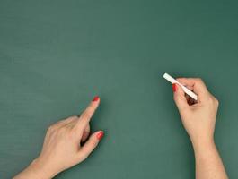 hand holds a piece of white chalk on the background of an empty green chalk board, presentation concept photo