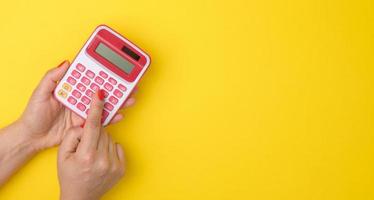 female hand holding a pink calculator on a yellow background, copy space photo