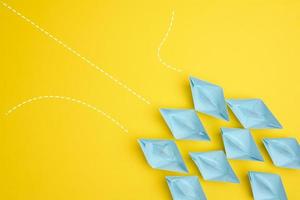 group of blue paper boats with different paths on yellow background, path choice concept. Teamwork photo