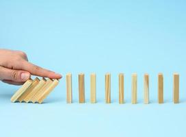 hand with a finger stops the fall of wooden bars on a blue background photo