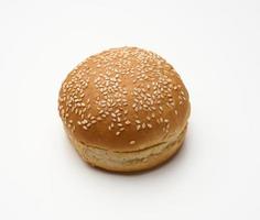 baked round fresh white wheat flour bun sprinkled with sesame seeds on a white table. Hamburger, cheeseberger and sandwich bun photo