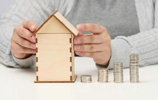 wooden model of a house, a stack of coins. The man sits at the table. Higher property prices, higher rents and higher mortgage interest rates photo