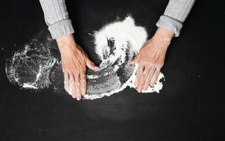 Sifted white wheat flour on a black table and two female hands, top view. cooking at home photo