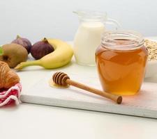 honey in a glass transparent jar and a wooden stick on a white table photo