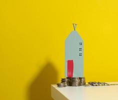 miniature wooden house and a stack of coins on a white table. Real estate purchase, mortgage concept. Rise in real estate prices, subsidies from the state photo