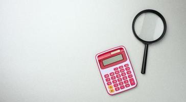 black plastic magnifier and pink calculator on gray background, budget planning, profit counting photo