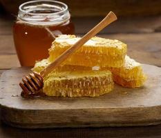 panal de cera con miel sobre una tabla de madera, detrás de un tarro de miel foto