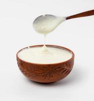 sour cream in a brown ceramic bowl with a wooden spoon on a white background photo