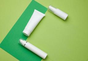 botella y tubos de plástico blancos vacíos para cosméticos sobre un fondo verde. envases para crema, gel, suero foto