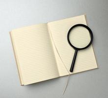 paper notebook with blank white sheets and a black magnifier on a gray background photo
