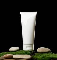 tubos de plástico blancos vacíos para soportes cosméticos sobre musgo verde, fondo negro. embalaje para crema, gel, suero, publicidad y promoción de productos, maqueta