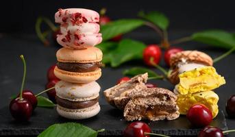 stack of multicolored macarons and ripe red cherries on black wooden background photo