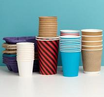 stack of paper disposable multi-colored cups and stand on white table, blue background photo