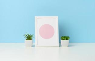 empty white wooden photo frame and flowerpots with plants on white table