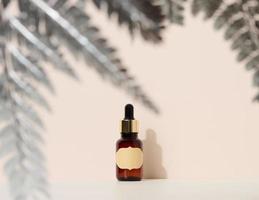 brown glass bottle with a pipette stands on a brown background. Container for cosmetics, serum and oil, silver fern leaf photo