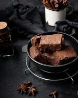 trozos horneados de pastel de brownie de chocolate con nueces en una sartén de metal negro sobre una mesa de madera, vista superior foto