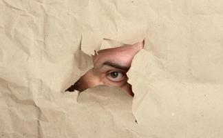 torn hole in brown paper with male peeping eye, man spying and peeping photo