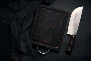 tabla de cortar de madera vacía rectangular y cuchillo de cocina sobre mesa negra con servilleta de gasa, vista superior foto