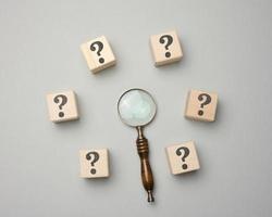 Wooden magnifier and cubes with question marks on gray background photo