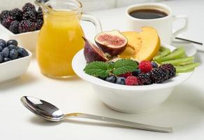 full plate with oatmeal and fruit, freshly squeezed juice in a transparent glass decanter, cup of coffee on a white table. Healthy breakfast photo