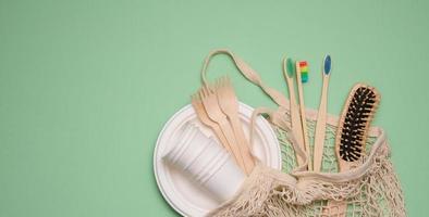 white cotton bag, paper cups and wooden toothbrushes on a green background, copy space photo