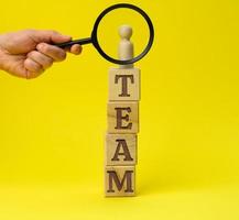 wooden figurine of a man on a pedestal and a hand with a magnifying glass on a yellow background. The concept of recruiting and finding talented employees photo