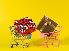 gift box with a red silk bow in a miniature metal trolley on a yellow background. Party Backdrop, surprise photo