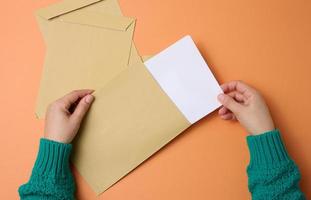 female hand holds paper envelopes on an orange background, top view. Correspondence photo