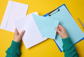 female hand holds white paper envelopes on an orange background, top view. Sending and receiving correspondence photo